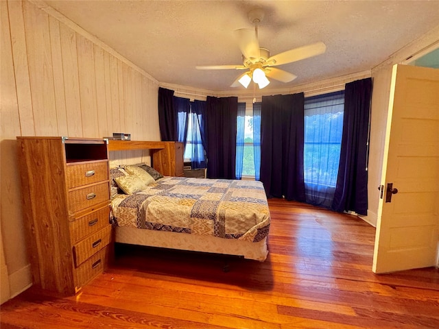900 Park Dr, Hillsboro, TX 76645 - bedroom with wood-type flooring, a textured ceiling, wood walls, and ceiling fan