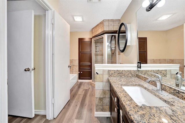full bath with vanity, a textured ceiling, wood finished floors, and a shower stall