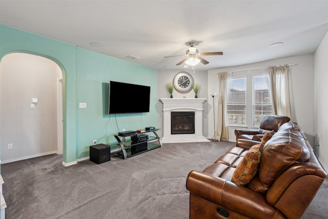 carpeted living room featuring ceiling fan, visible vents, arched walkways, baseboards, and a glass covered fireplace