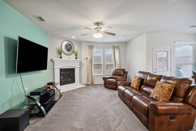 living room featuring a glass covered fireplace, ceiling fan, carpet flooring, and visible vents