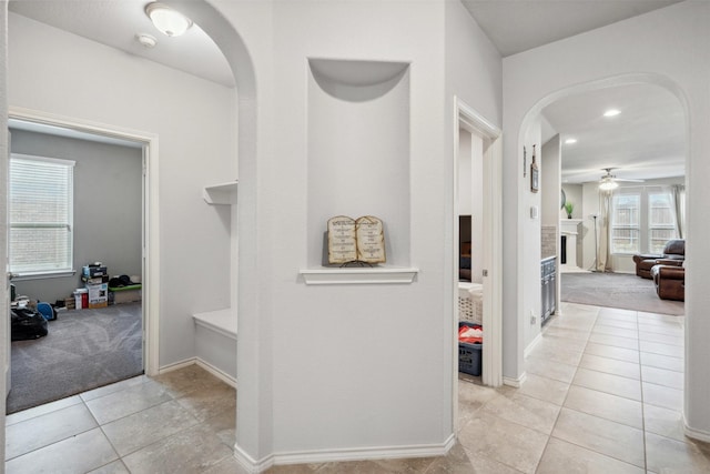 corridor with arched walkways, baseboards, recessed lighting, and light tile patterned floors