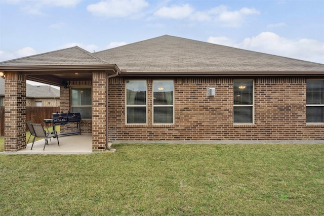 back of property with fence, brick siding, a shingled roof, a patio area, and a lawn