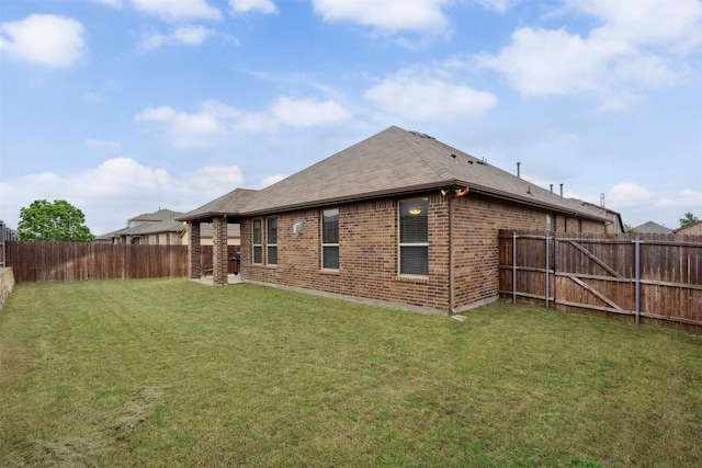 rear view of house with brick siding, a fenced backyard, a yard, and a shingled roof