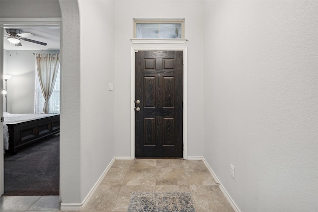 foyer with baseboards, a ceiling fan, and stone finish flooring
