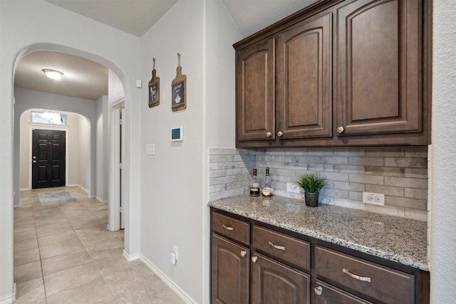 bar featuring baseboards, arched walkways, light tile patterned floors, and backsplash