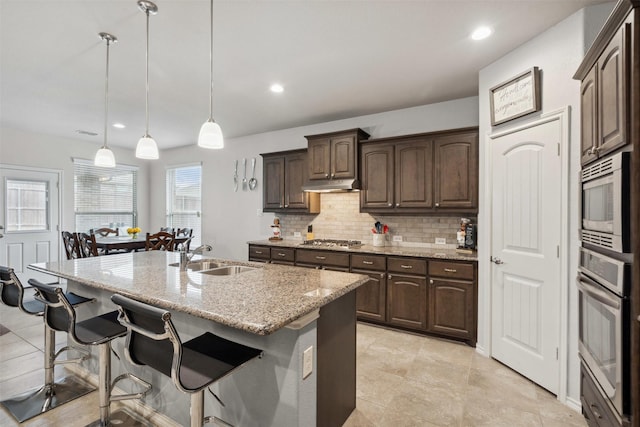 kitchen featuring a breakfast bar, under cabinet range hood, tasteful backsplash, a sink, and stainless steel appliances
