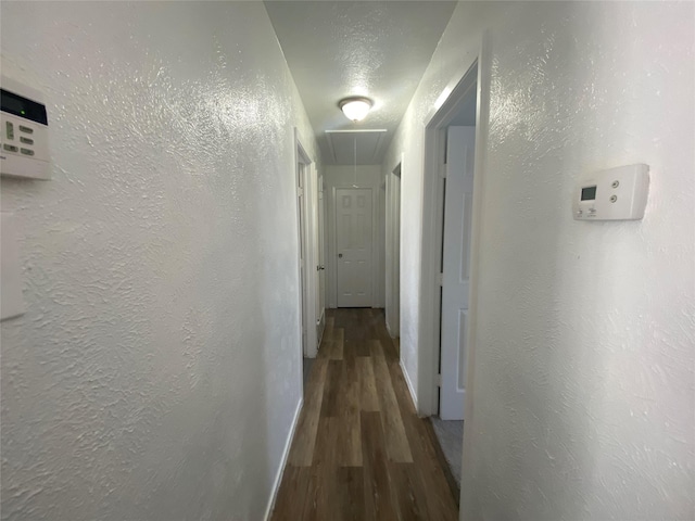 hallway featuring baseboards, a textured wall, wood finished floors, and attic access