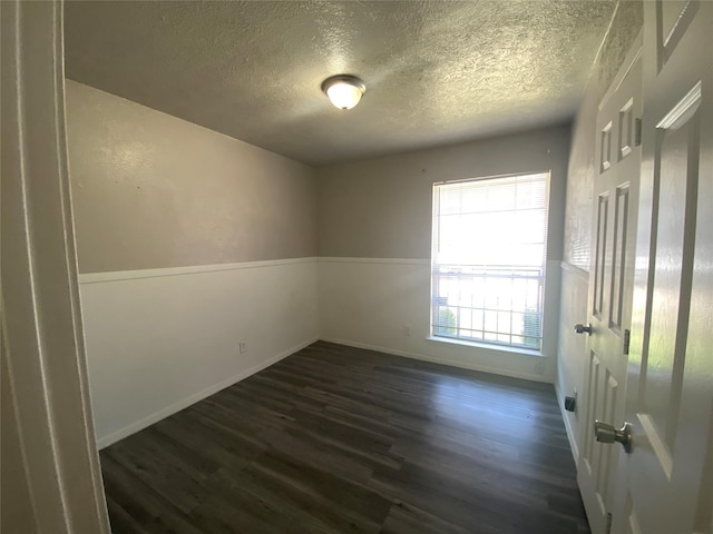 spare room with dark wood-type flooring, a textured ceiling, and baseboards