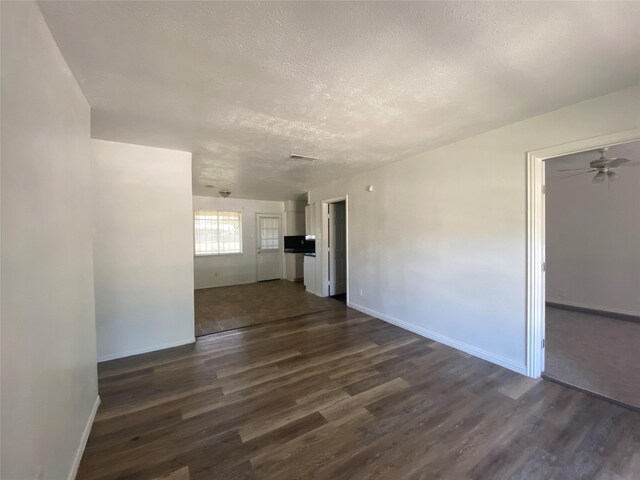 unfurnished living room featuring dark wood-type flooring, a textured ceiling, ceiling fan, and baseboards