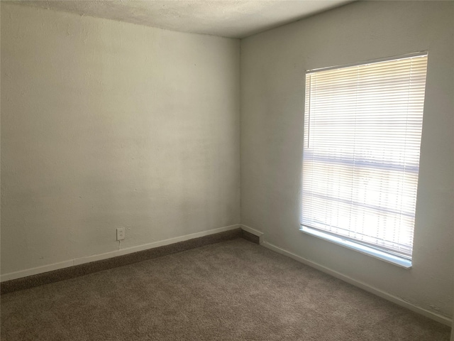 empty room featuring baseboards and dark carpet