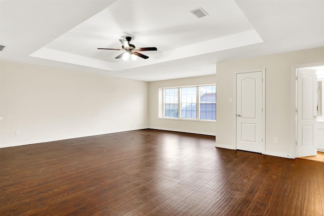 spare room featuring a ceiling fan, a tray ceiling, dark wood-type flooring, and visible vents