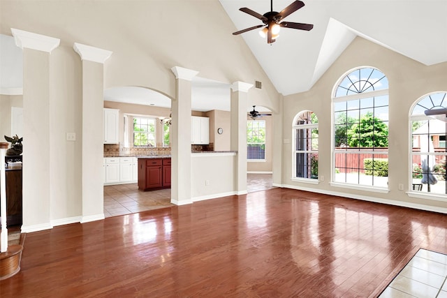 unfurnished living room featuring a ceiling fan, arched walkways, light wood-type flooring, a sink, and high vaulted ceiling
