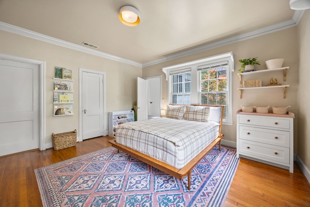 bedroom featuring crown molding, light wood finished floors, and visible vents