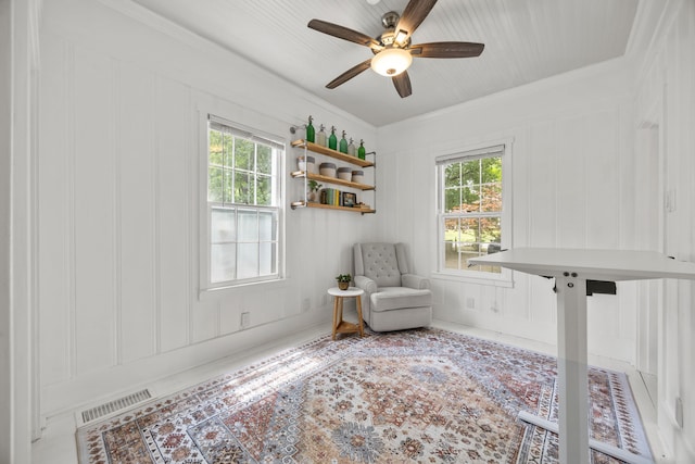 living area with ceiling fan, visible vents, a wealth of natural light, and a decorative wall
