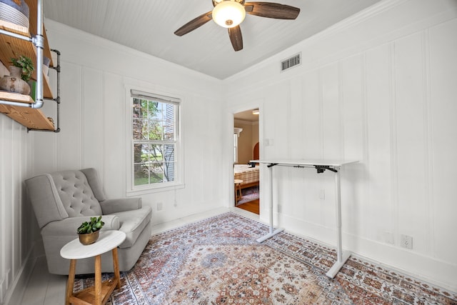 sitting room featuring visible vents, a ceiling fan, crown molding, and a decorative wall