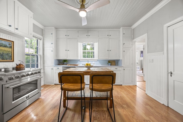 kitchen featuring stainless steel stove, white cabinetry, light wood finished floors, and ceiling fan