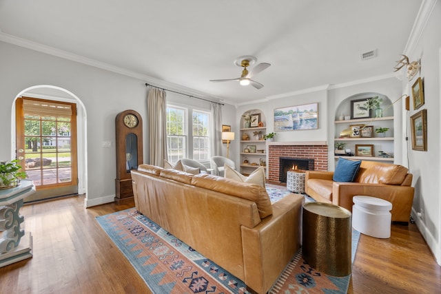 living area with ornamental molding, wood finished floors, a fireplace, arched walkways, and a ceiling fan