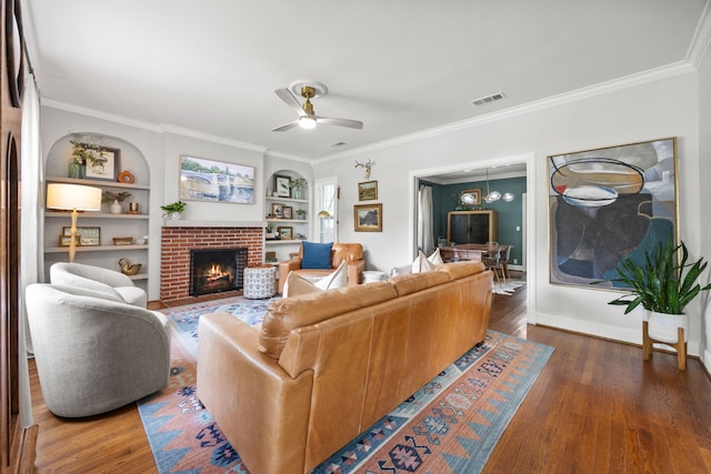 living area with visible vents, ornamental molding, built in features, a fireplace, and ceiling fan