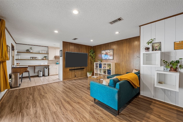 living room featuring a textured ceiling, visible vents, wooden walls, light wood-style floors, and recessed lighting