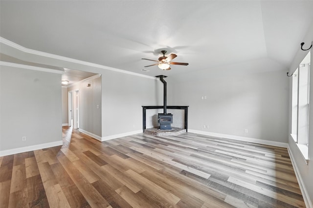 unfurnished living room with baseboards, a ceiling fan, a wood stove, and light wood-style flooring