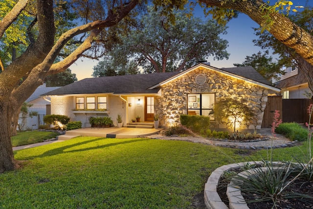 single story home featuring a yard, fence, and stone siding