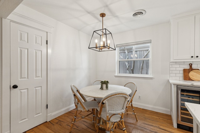 dining space featuring visible vents, an inviting chandelier, wine cooler, baseboards, and light wood-style floors
