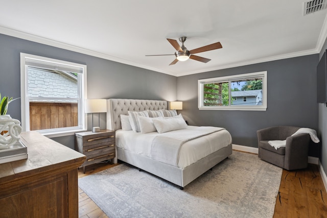 bedroom featuring ceiling fan, wood-type flooring, baseboards, visible vents, and ornamental molding