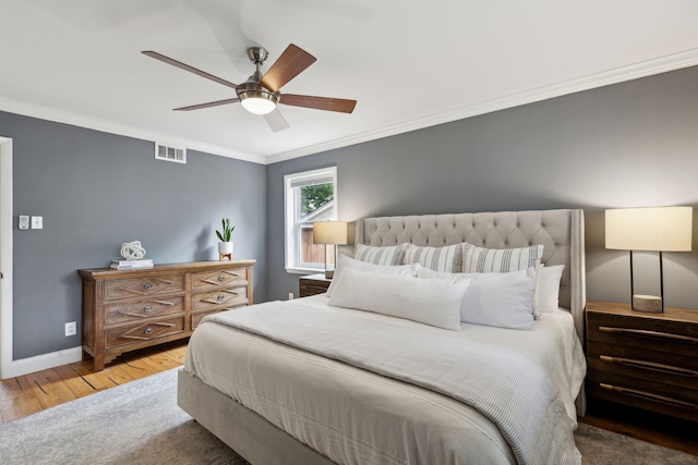 bedroom with visible vents, ornamental molding, wood finished floors, baseboards, and a ceiling fan