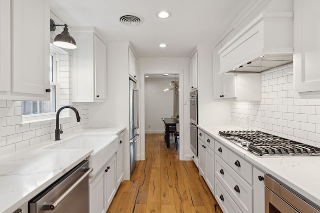 kitchen featuring visible vents, white cabinets, custom range hood, a sink, and appliances with stainless steel finishes