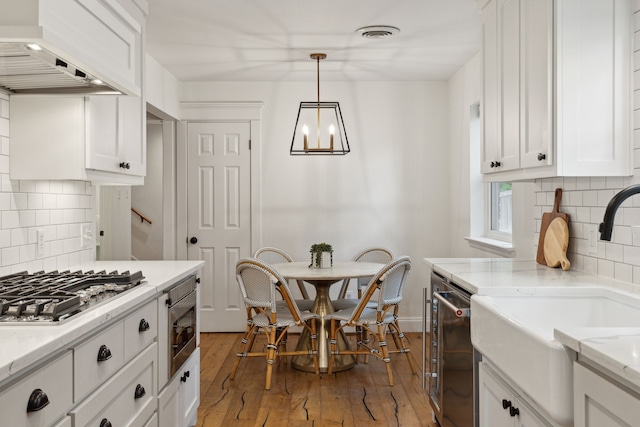 kitchen featuring appliances with stainless steel finishes, a sink, white cabinets, a chandelier, and custom range hood
