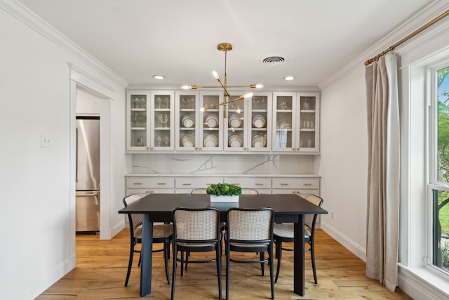 dining space with an inviting chandelier, ornamental molding, light wood-style flooring, and visible vents