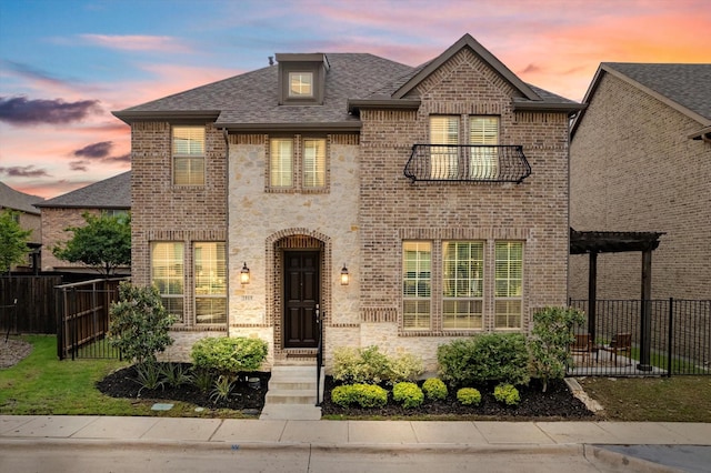 view of front of property featuring fence, brick siding, a balcony, and a shingled roof