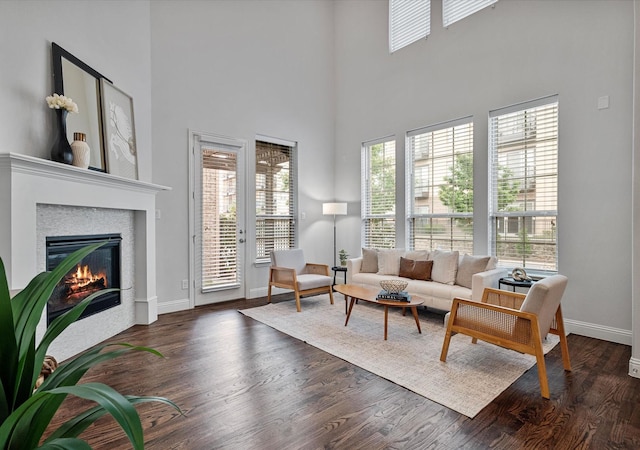 living room featuring a towering ceiling, baseboards, dark wood finished floors, and a glass covered fireplace