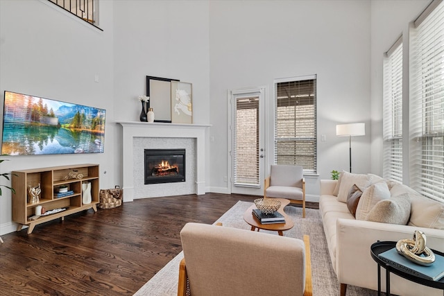 living room with a high ceiling, a glass covered fireplace, wood finished floors, and baseboards
