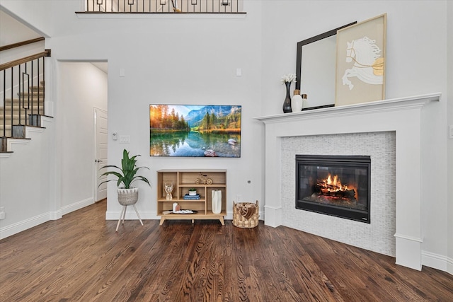 living area featuring wood finished floors, stairs, a high ceiling, a glass covered fireplace, and baseboards