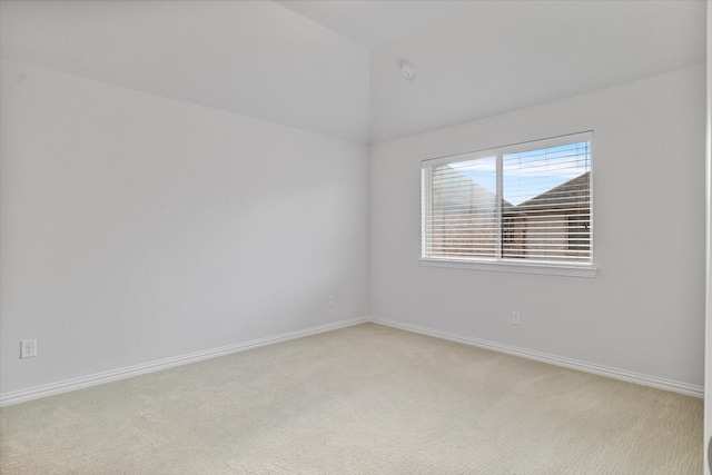 empty room with light colored carpet, vaulted ceiling, and baseboards