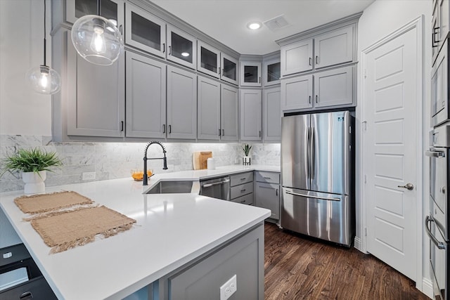 kitchen featuring stainless steel appliances, gray cabinets, a peninsula, a sink, and dark wood-style floors