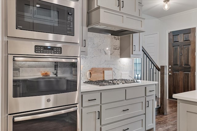 kitchen featuring appliances with stainless steel finishes, tasteful backsplash, ornamental molding, custom exhaust hood, and light countertops