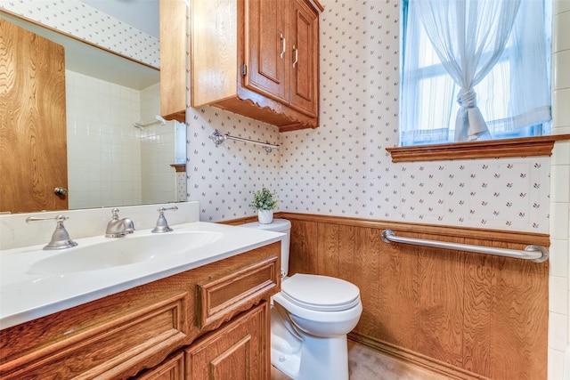 full bath with walk in shower, vanity, toilet, a wainscoted wall, and wallpapered walls