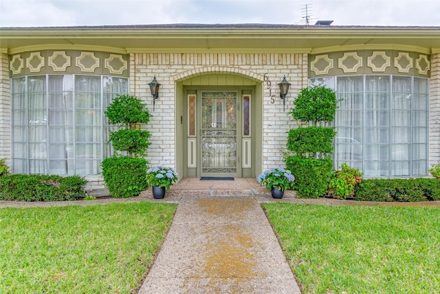entrance to property featuring a yard and brick siding