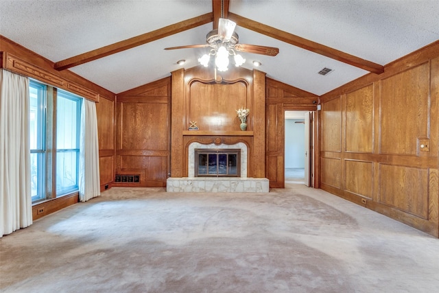 unfurnished living room with visible vents, a glass covered fireplace, ceiling fan, wooden walls, and lofted ceiling with beams