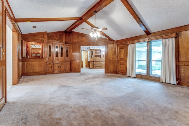 unfurnished living room with ceiling fan, a textured ceiling, light colored carpet, lofted ceiling with beams, and wooden walls