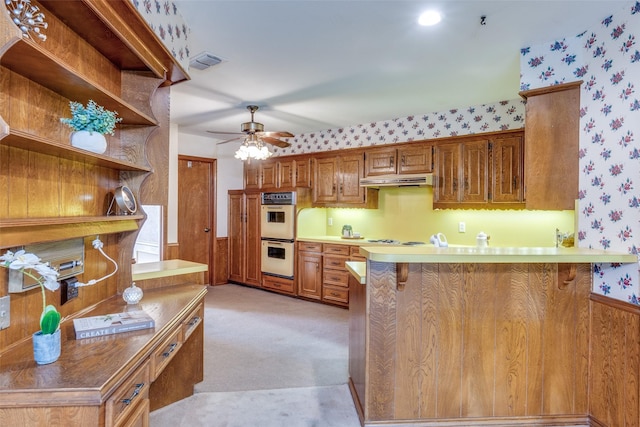 kitchen featuring a ceiling fan, visible vents, white double oven, a peninsula, and wallpapered walls