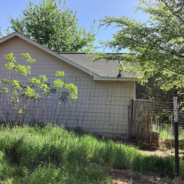 view of side of home with fence and a shingled roof