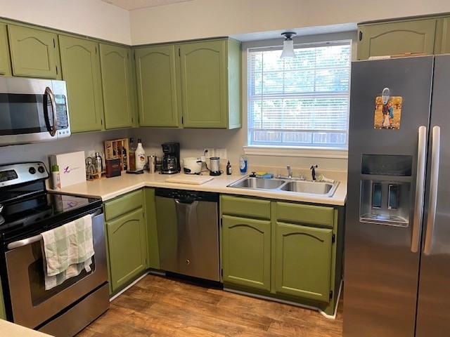 kitchen featuring wood finished floors, light countertops, a sink, green cabinets, and stainless steel appliances