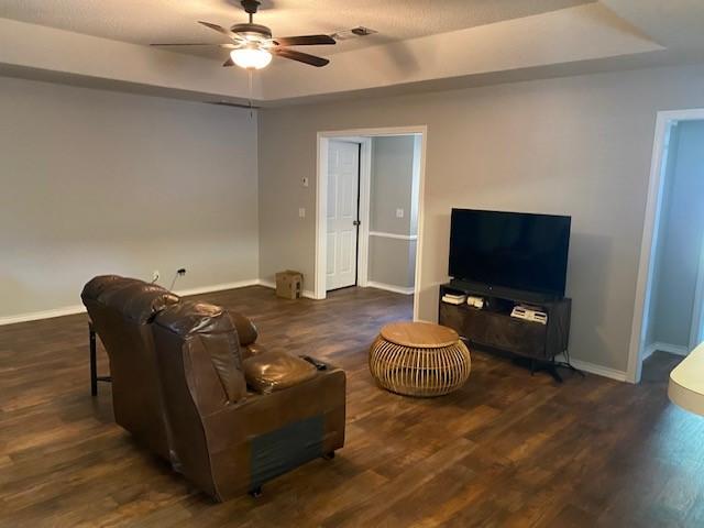 living area with a ceiling fan, a tray ceiling, and baseboards