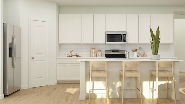 kitchen with backsplash, light wood-style floors, light countertops, white cabinets, and appliances with stainless steel finishes