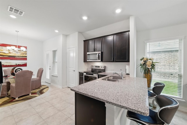 kitchen featuring visible vents, appliances with stainless steel finishes, a sink, light stone counters, and a notable chandelier