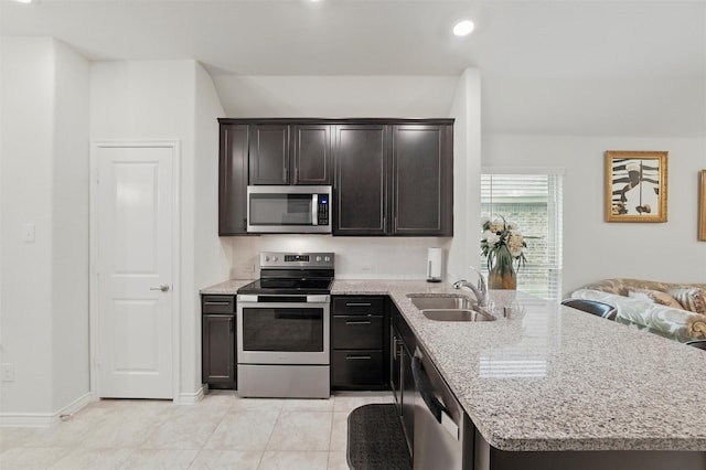 kitchen featuring appliances with stainless steel finishes, light stone counters, a sink, a peninsula, and light tile patterned floors