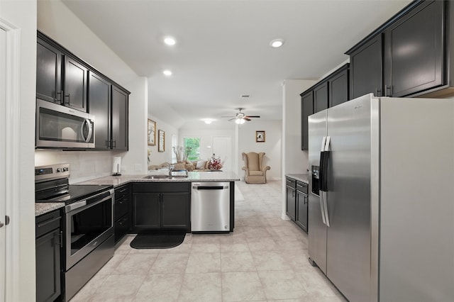 kitchen with a sink, open floor plan, light stone counters, a ceiling fan, and appliances with stainless steel finishes